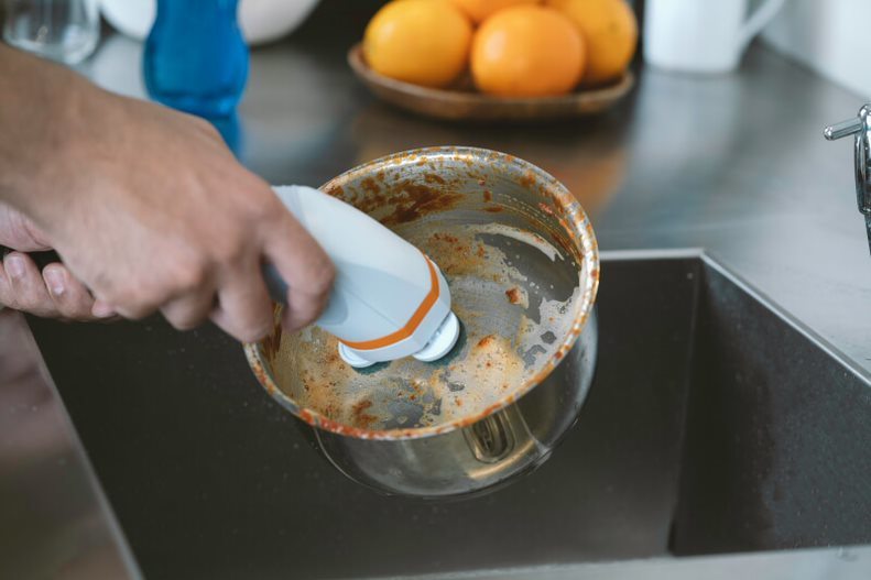 Ice blue scrub brush scrubbing a metal pot on a stovetop