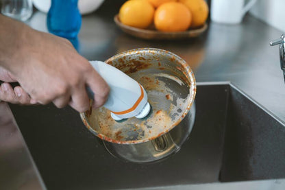 Ice blue scrub brush scrubbing a metal pot on a stovetop