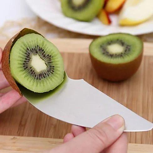 Kiwi slicing tool with long white blade, held near halved kiwi on wooden board