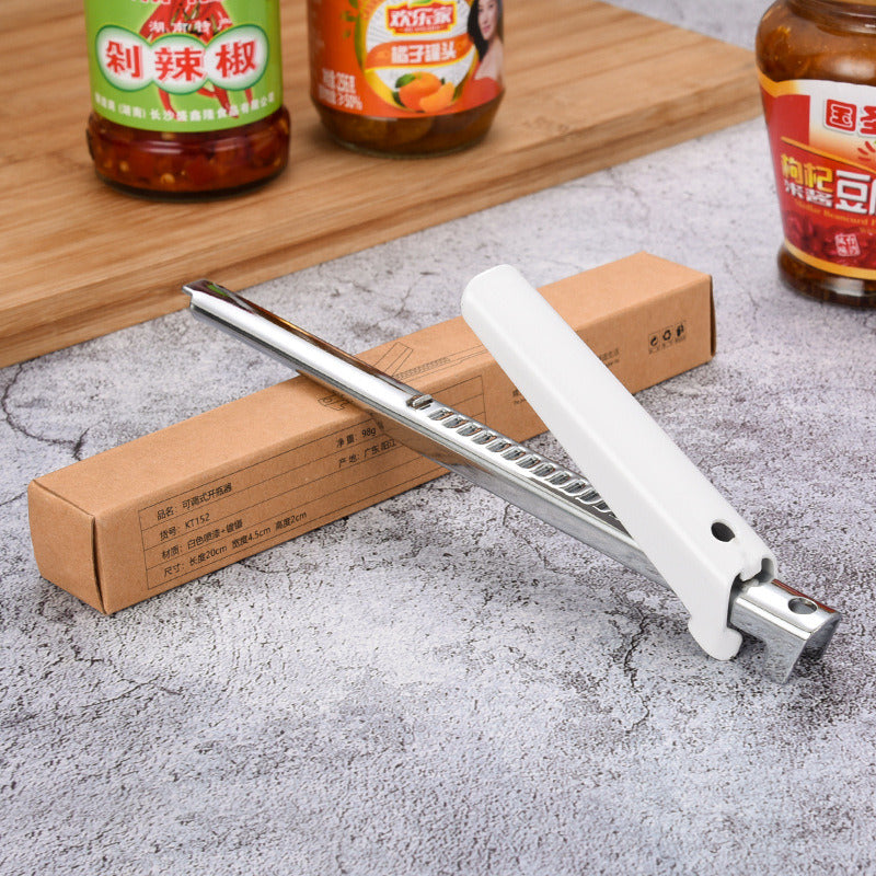 Jar lid opener with white handle and long stainless grip across cardboard boxes on counter.
