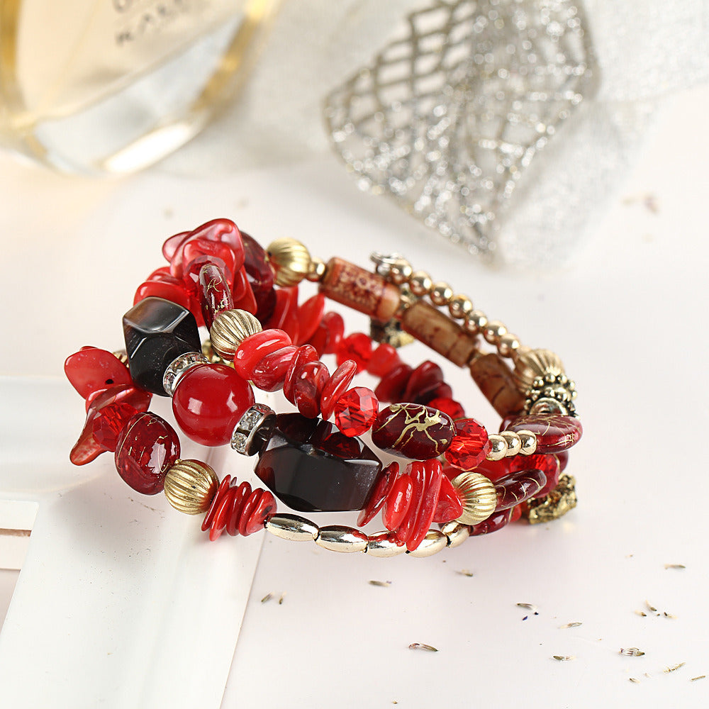 Red boho charm bracelet with red and black beads, gold-tone spacers, and flower charm drops.