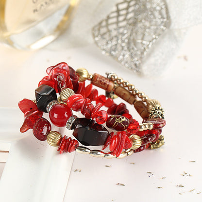 Red boho charm bracelet with red and black beads, gold-tone spacers, and flower charm drops.