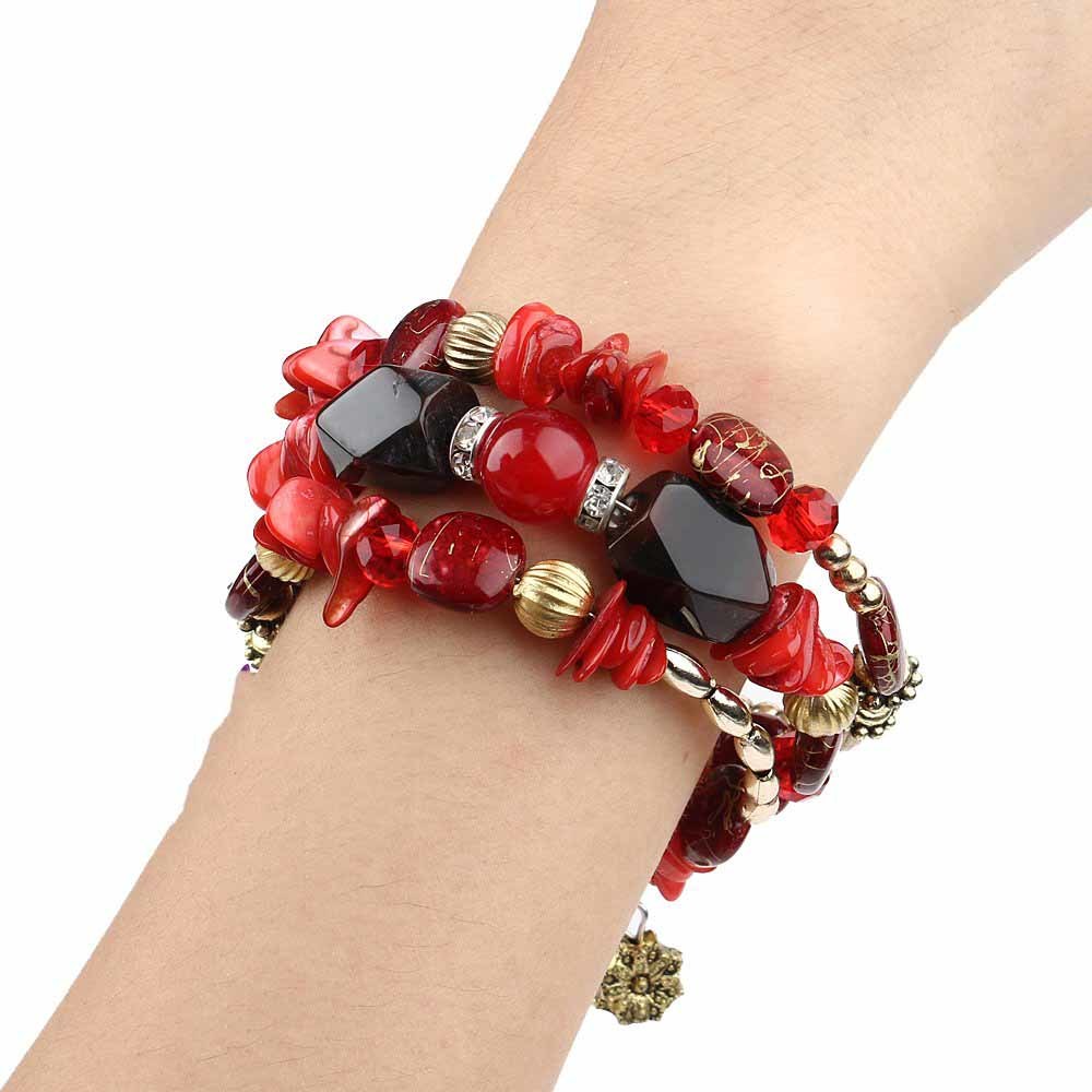 Red boho charm bracelet on wrist with red chip beads, black stone pieces, and gold rings.