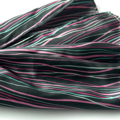 Silky scarf fabric close-up with dark base and thin pink and teal irregular stripes