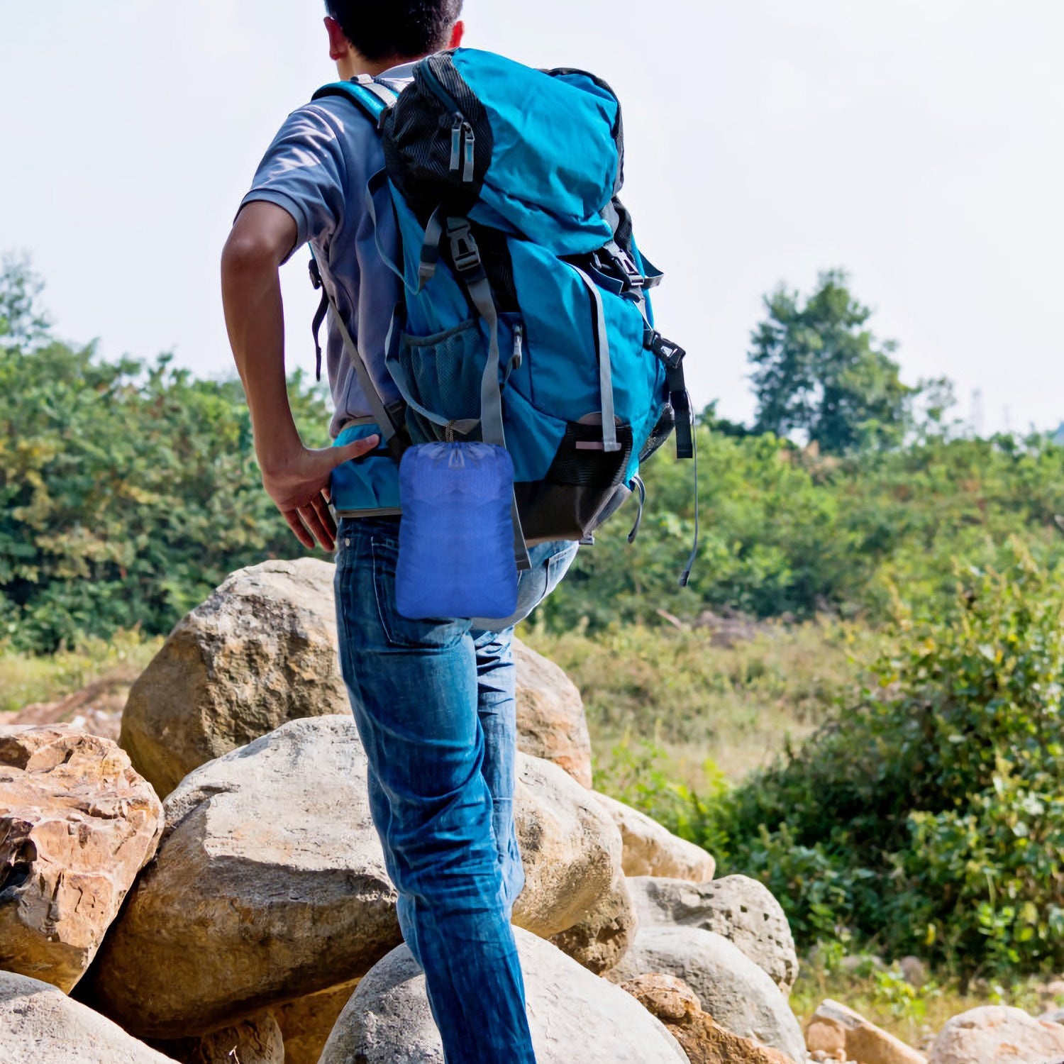 Person carrying a blue hammock in a backpack-style carry bag on rocks
