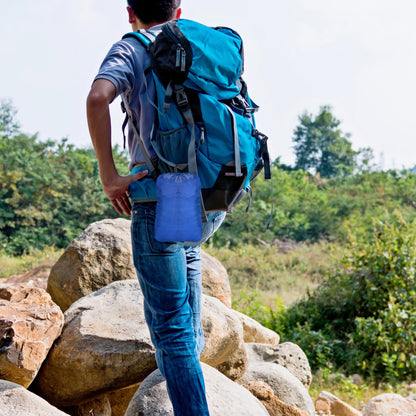 Person carrying a blue hammock in a backpack-style carry bag on rocks