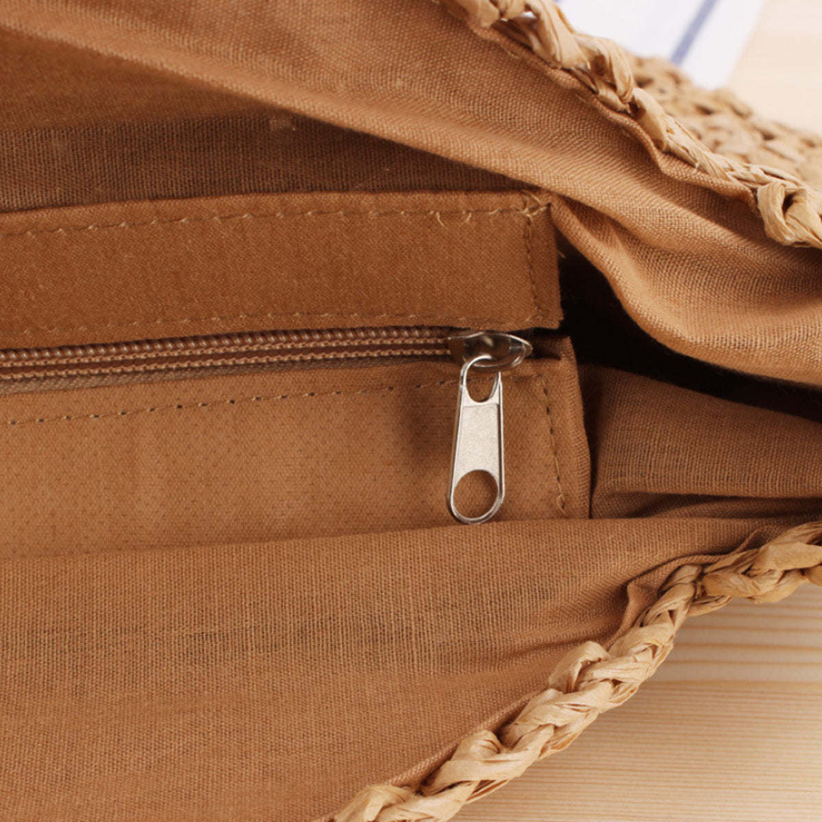 Tan fabric lining inside tote with metal zipper pull and braided straw edge