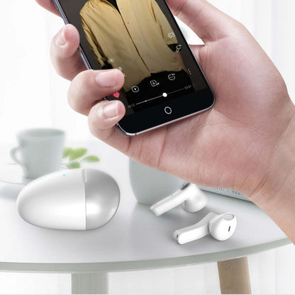 White twin Bluetooth earbuds near smartphone in hand for wireless connection
