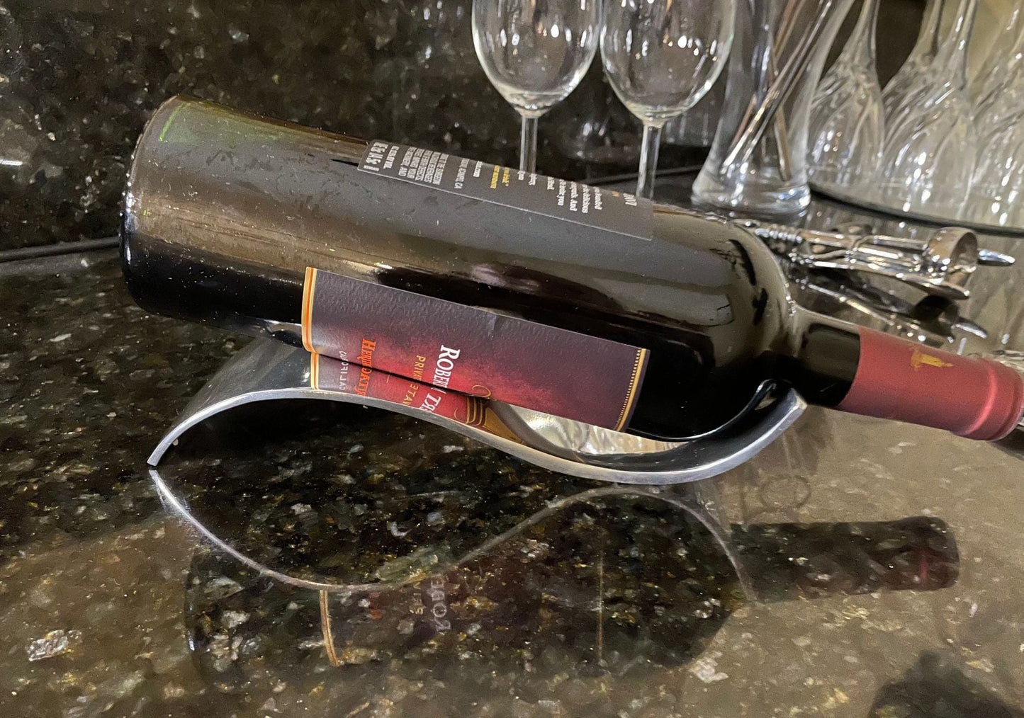 Curved chrome bottle holder with open cradle holding a dark wine bottle