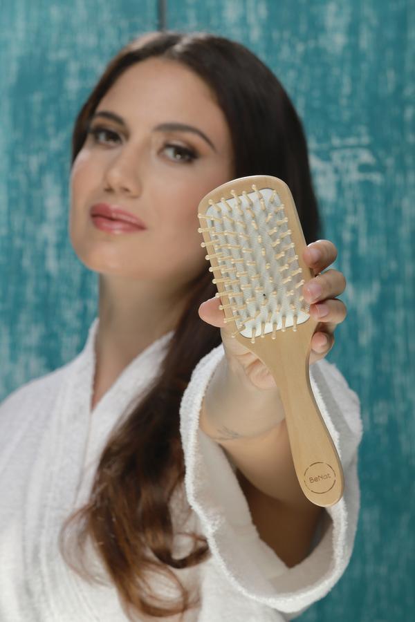 Natural wooden hair detangling brush held in hand with white pin bristles