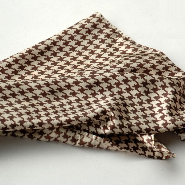 Silk scarf close-up with brown-and-cream houndstooth pattern and folded pointed tip