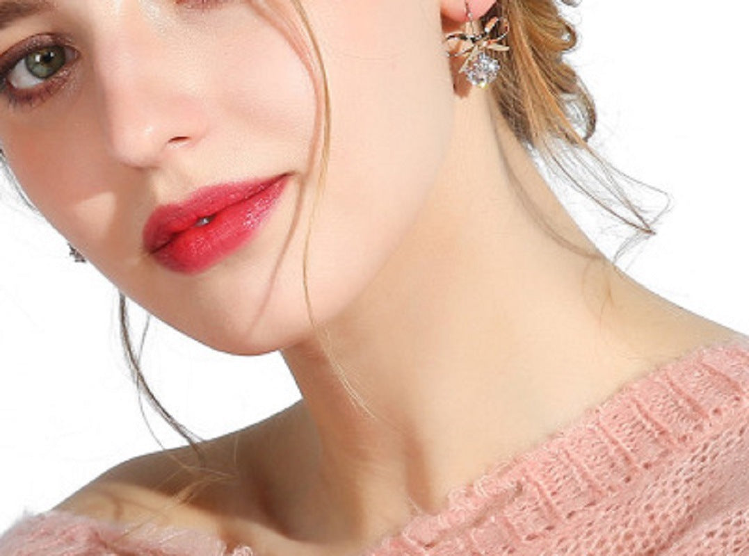 Gold-tone bow earrings with a round zircon stone, worn on the ear