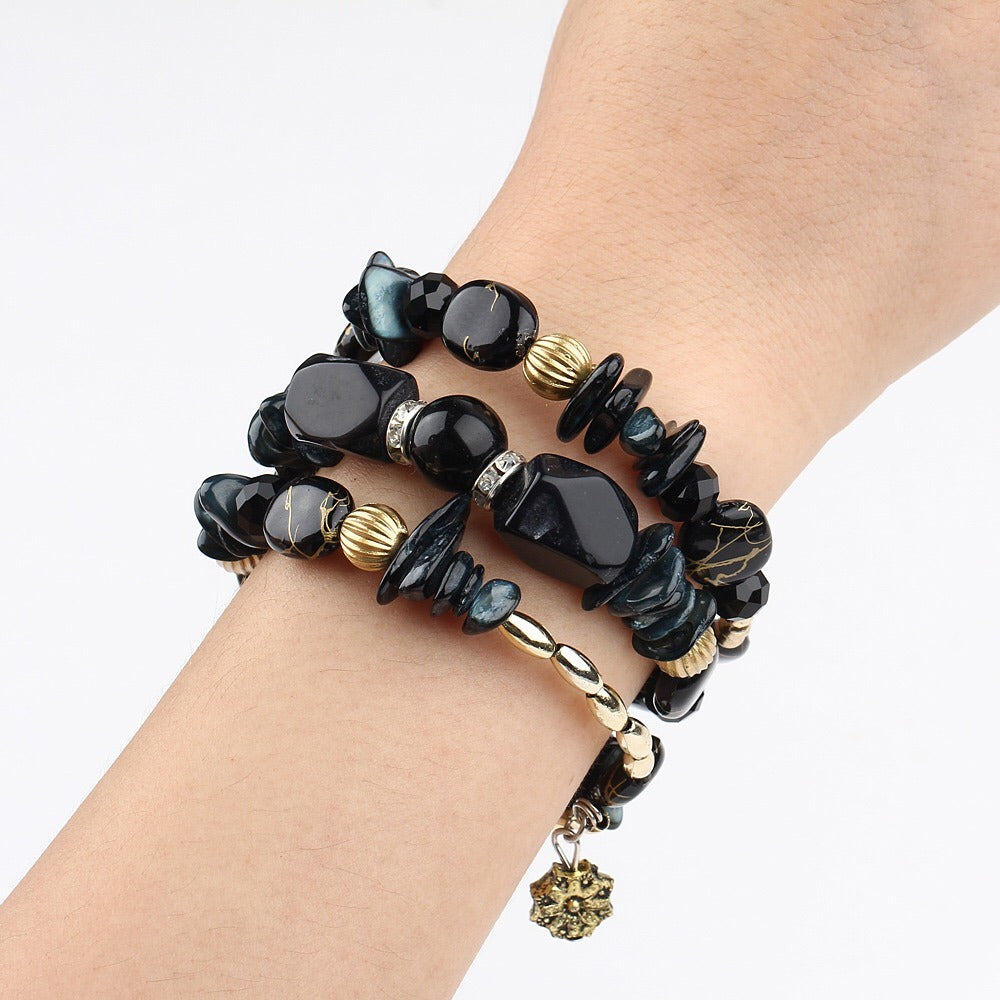 Multilayer boho charm bracelet on wrist with black beads, gold links, and small charm