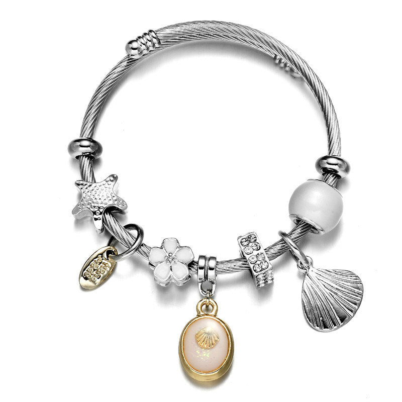 Silver wrap bangle bracelet with white bead, seashell fan, and gold-edged oval charm