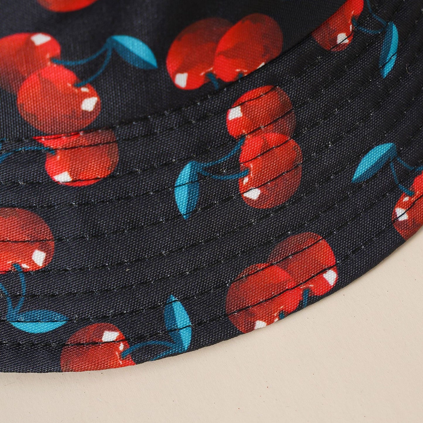Double-sided cherry bucket hat fabric close-up, dark with red cherries and blue leaves