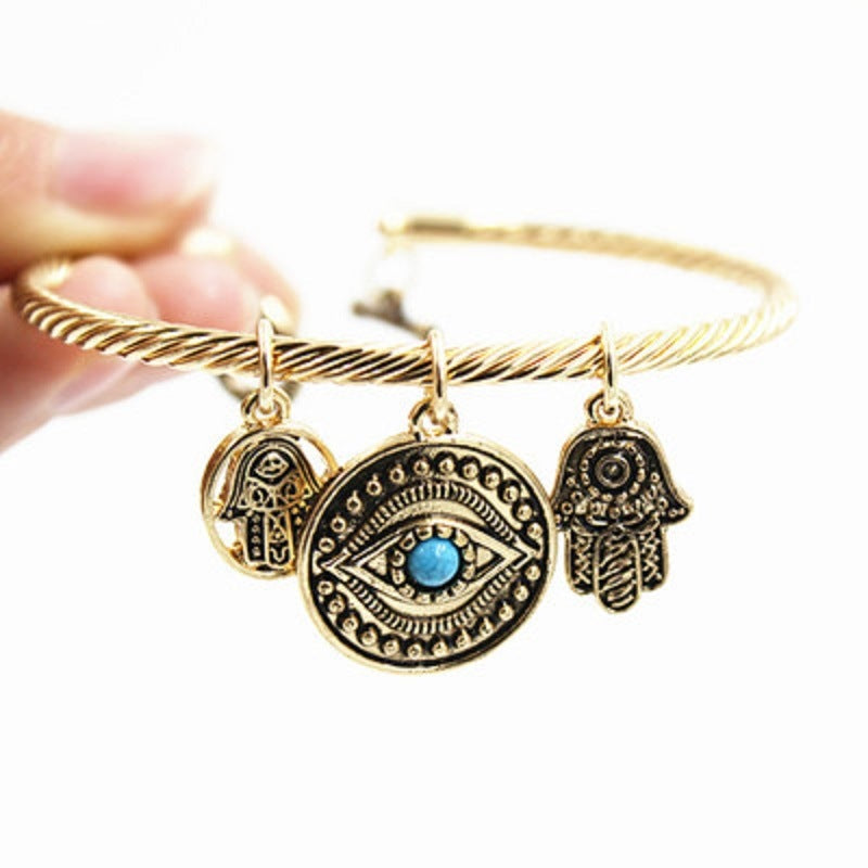Gold-tone twisted charm bracelet with evil eye and hamsa charms, blue enamel center details.