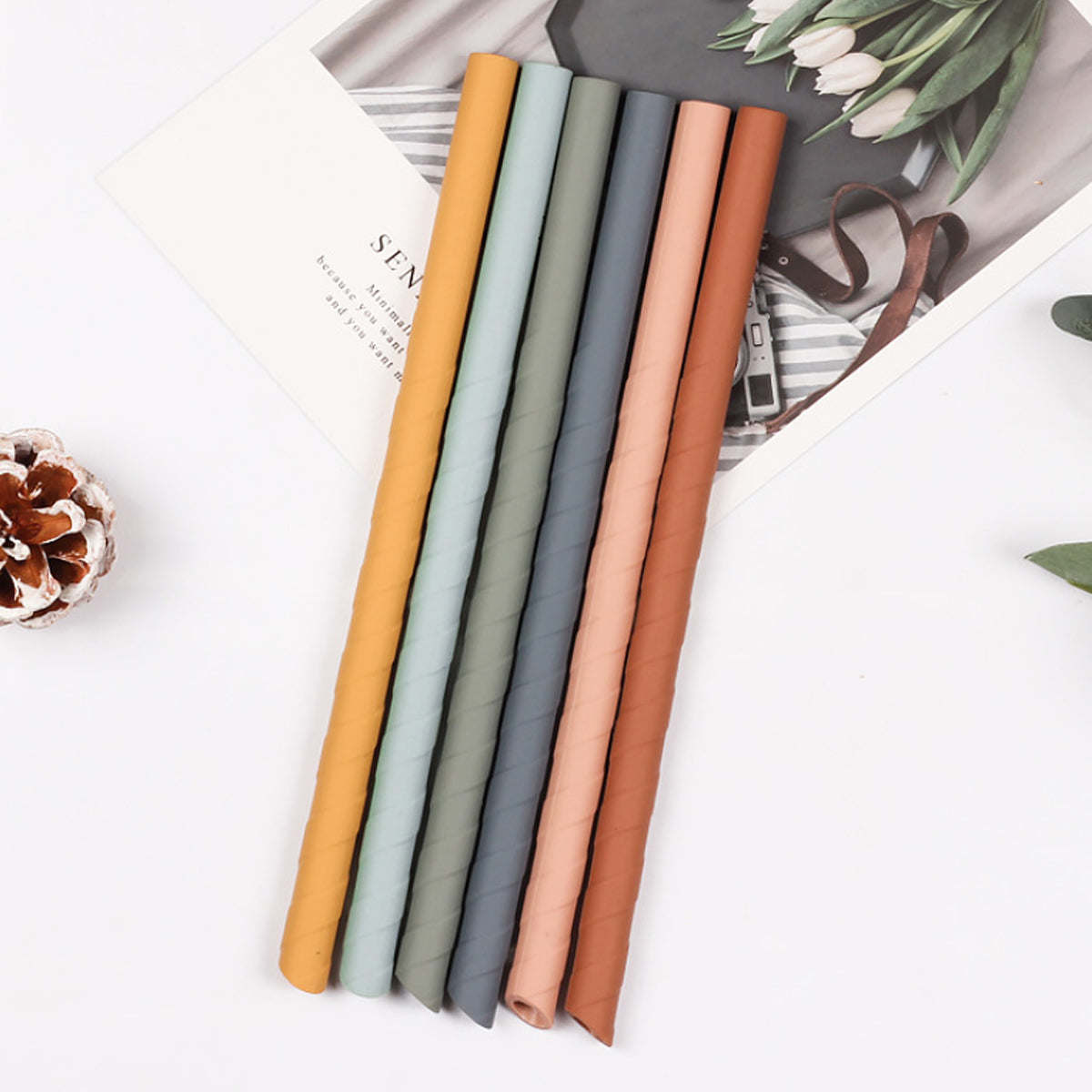 Reusable silicone straws in mustard, gray, pink, and sage laid on white surface