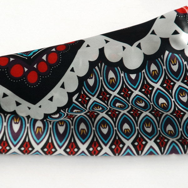 Close-up scarf fabric with circular and diamond motifs in black, white, red, and teal