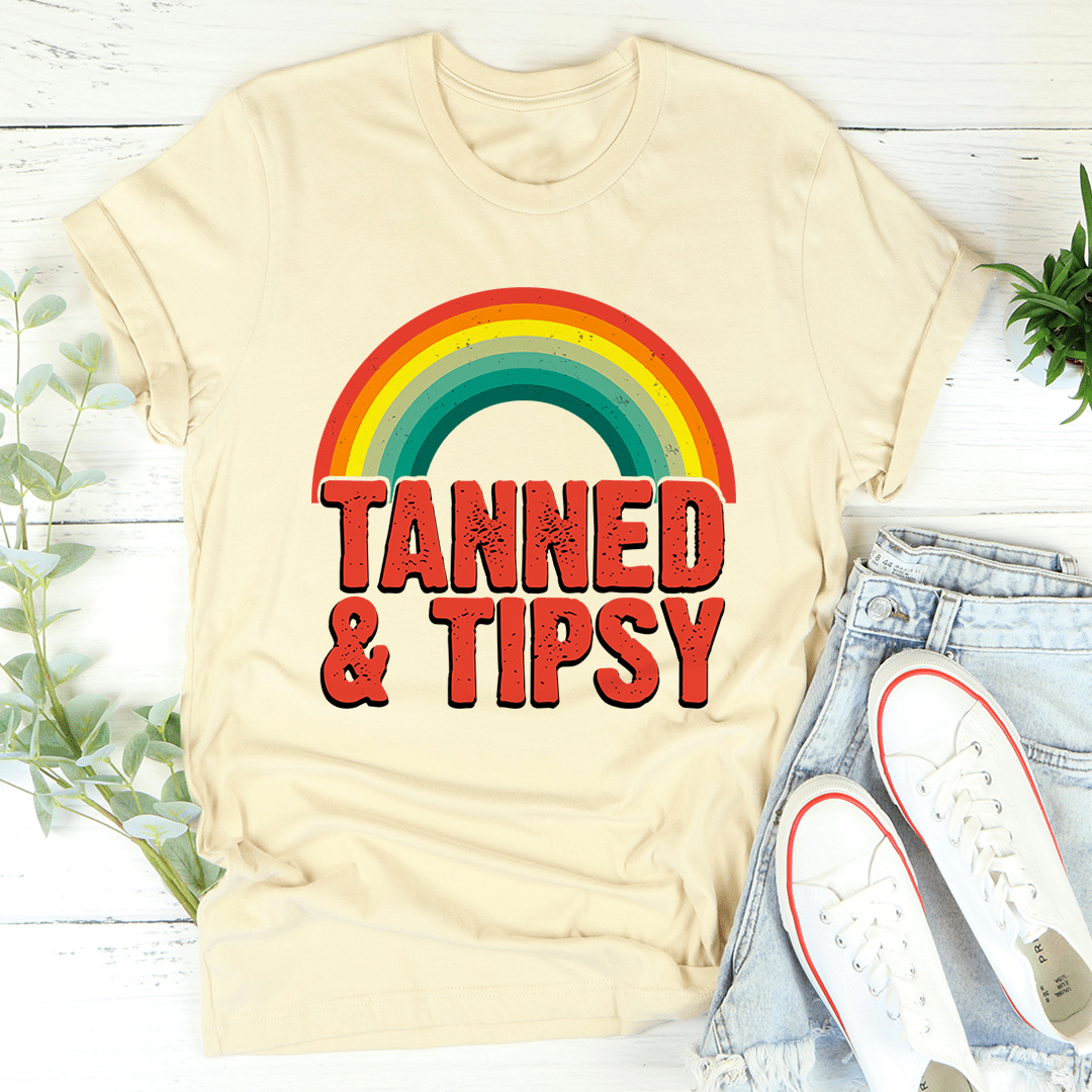 Cream T-shirt with rainbow arc and bold 'TANNED & TIPSY' lettering