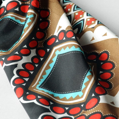 Silky scarf close-up: black fabric with red circles, teal shapes, and white patterned trim.