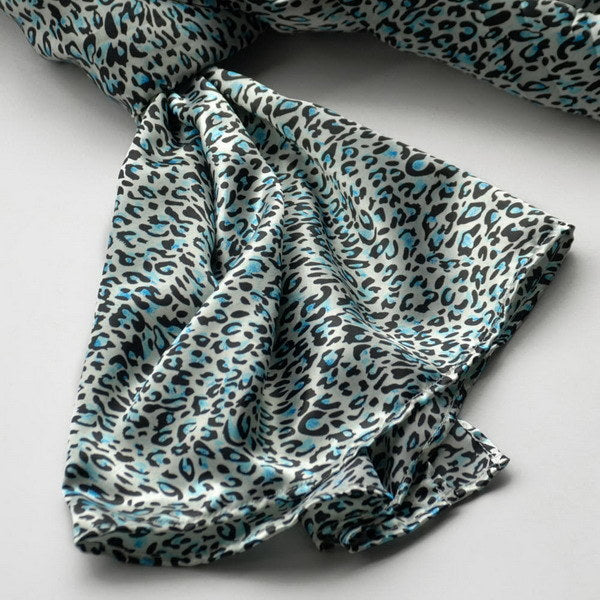 Sky blue leopard-print silk scarf close-up with swirling pattern and folds.