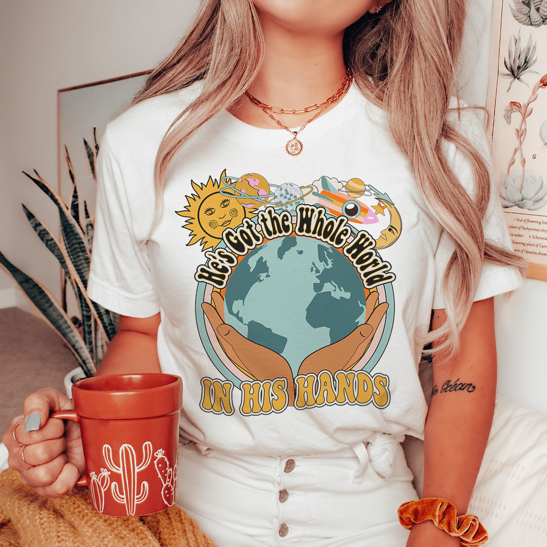 White T-shirt with globe-in-hands print and “IN HIS HANDS” lettering on front
