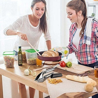 Garlic press in use on a kitchen table with two people preparing food.
