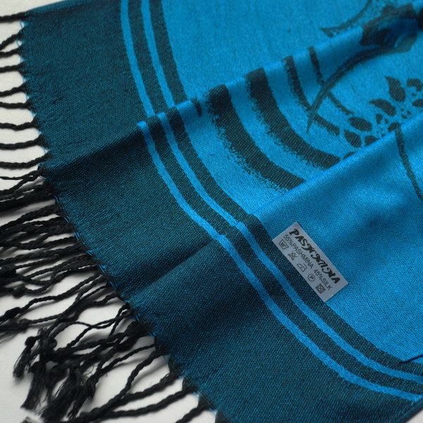 Blue patterned shawl with fringe tassels and a sewn label near the edge