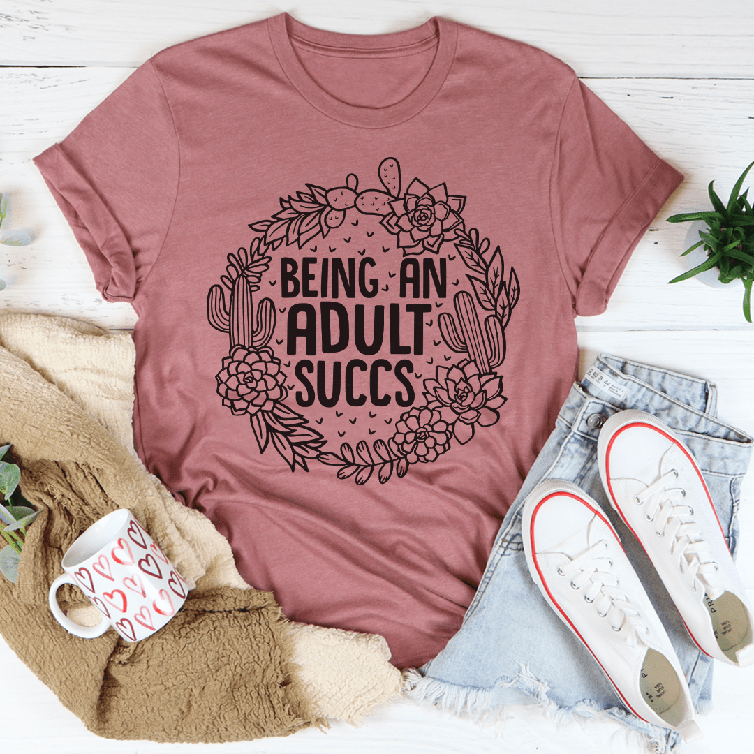 Mauve cactus-and-flower graphic T-shirt with bold Being an Adult Succs text