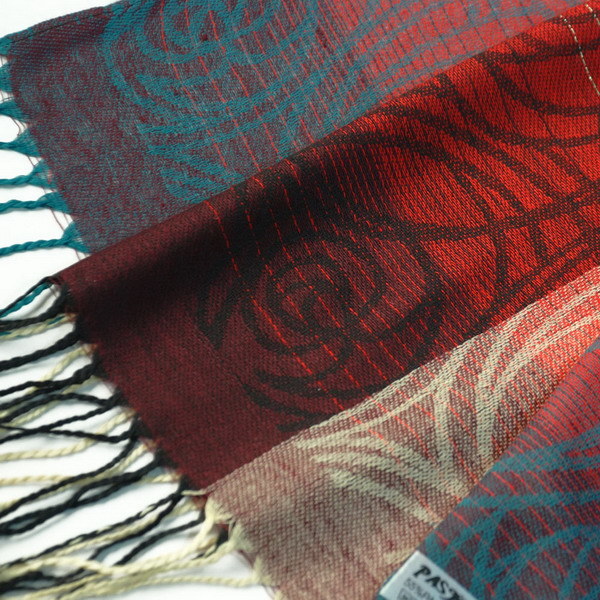 Pashmina scarf close-up with woven red and teal pattern, fringes and tassel detail.