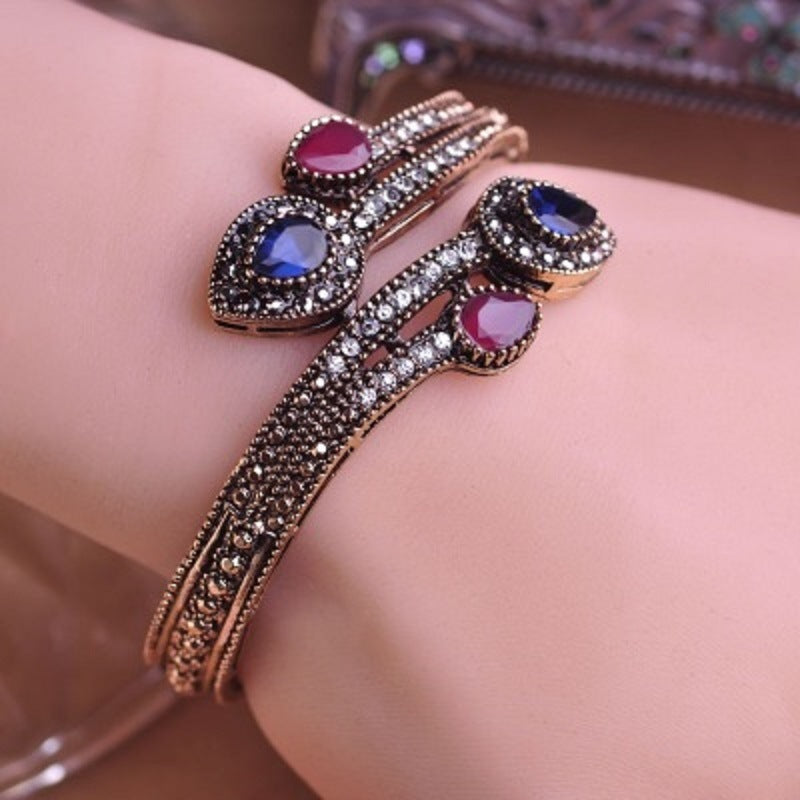 Rose-gold tone bypass bangle on wrist with blue and pink oval stones and clear CZ accents