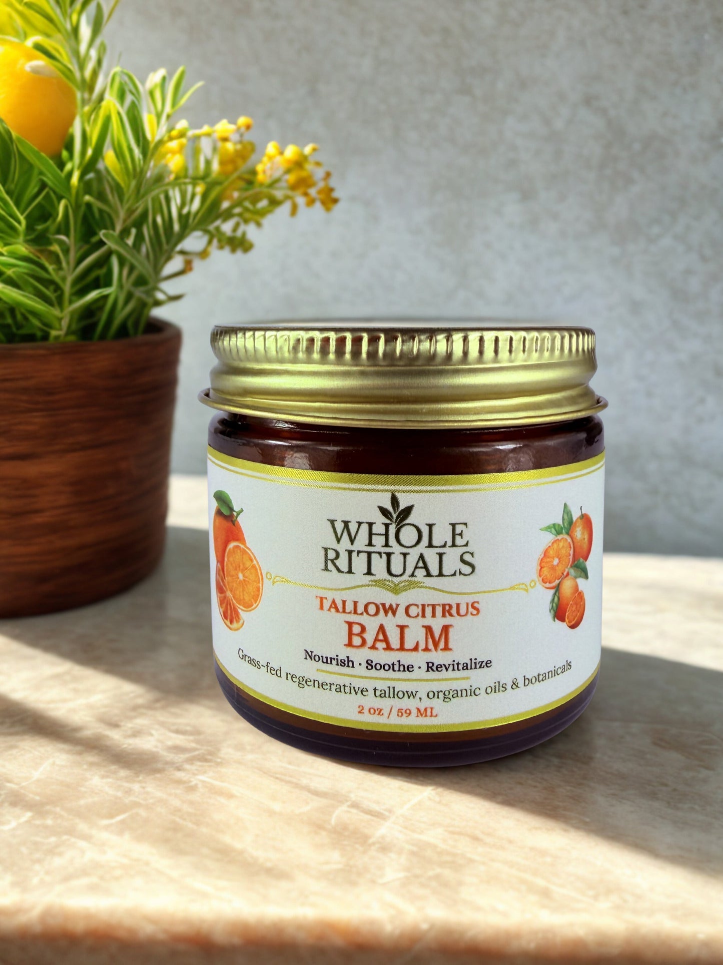 Tallow citrus balm jar with gold lid and citrus label, beside flowers in a wooden pot