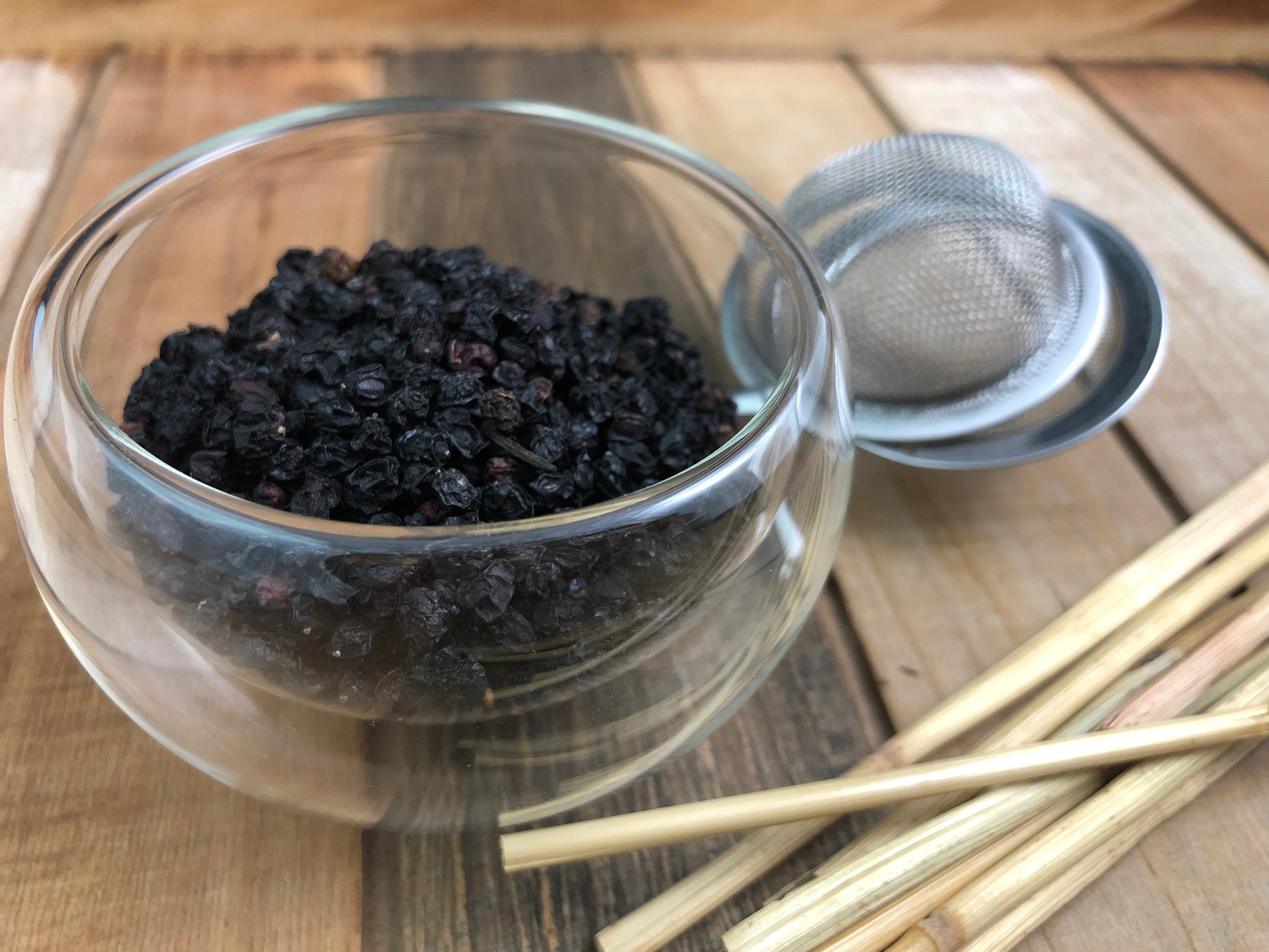 Organic elderberry dried berries in glass bowl with metal strainer and wooden scoops