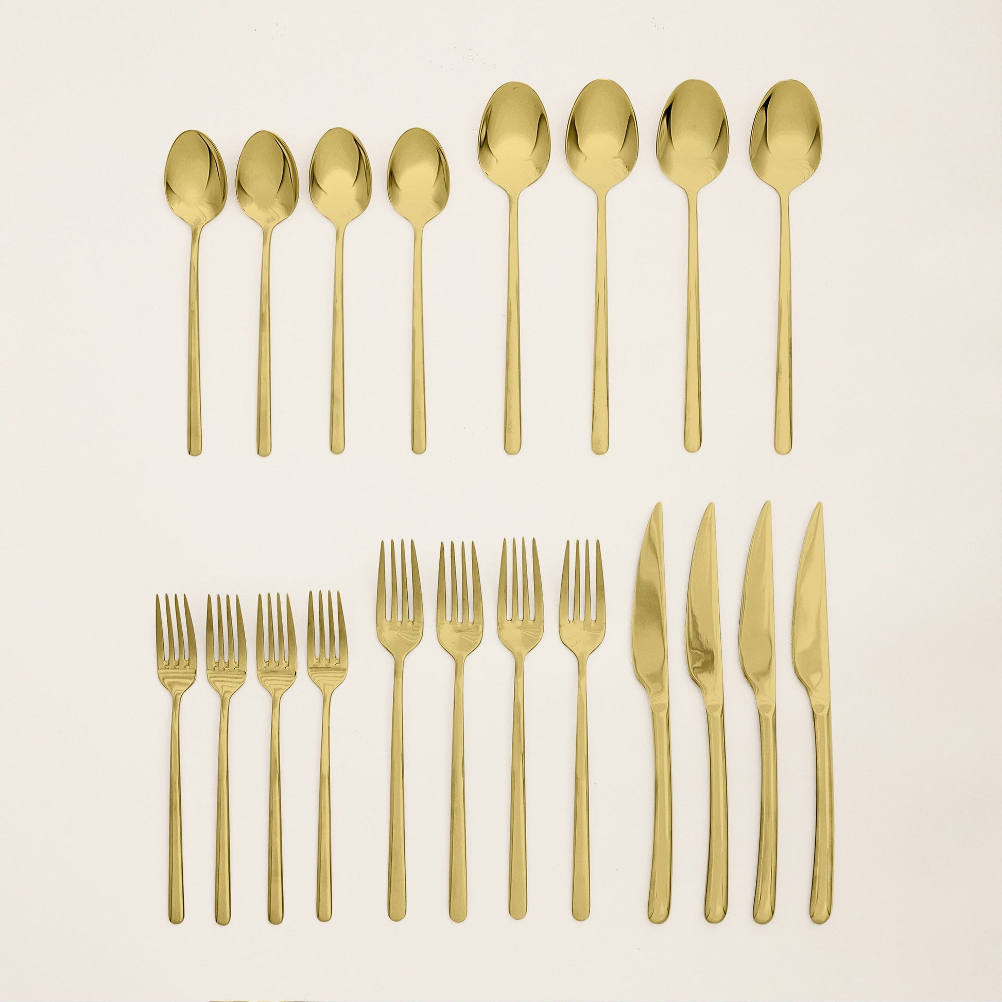 Gold flatware set pieces laid out: spoons, forks, and knives on a light surface