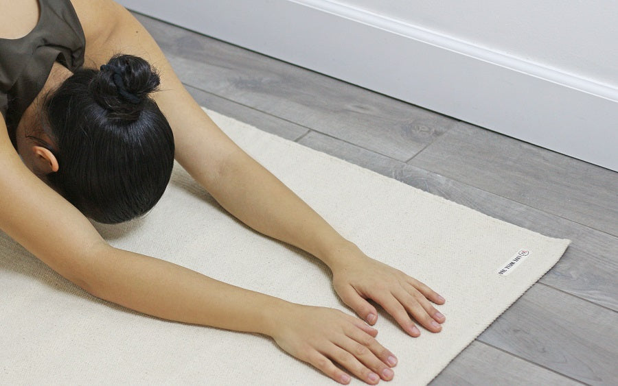 Organic cotton yoga mat in light cream, with hands resting on top during yoga.