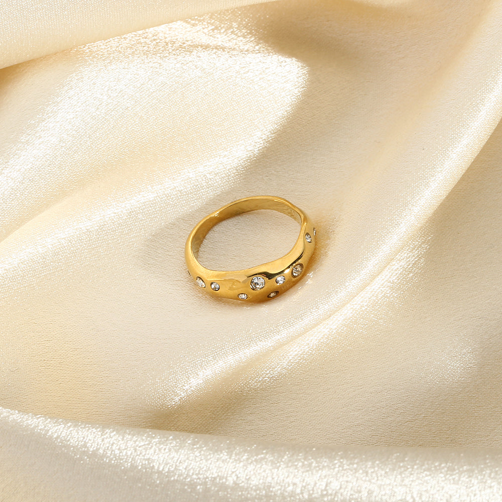 Gold snake-shape ring with clear stones, angled view on light fabric