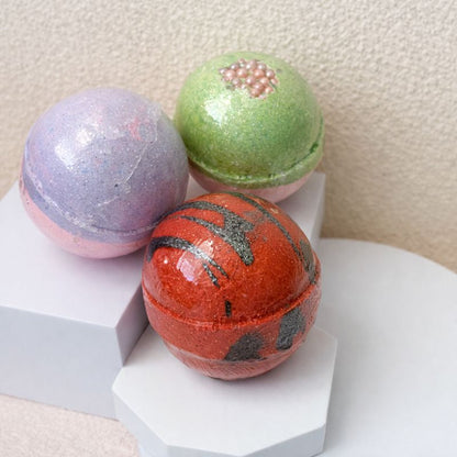Bath bomb box with lavender, green, and orange spherical bath bombs on white risers