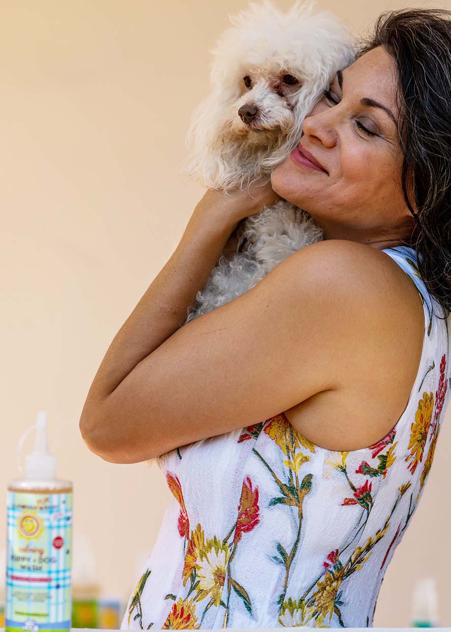 Calming puppy and dog wash bottle on counter with woman holding small white dog