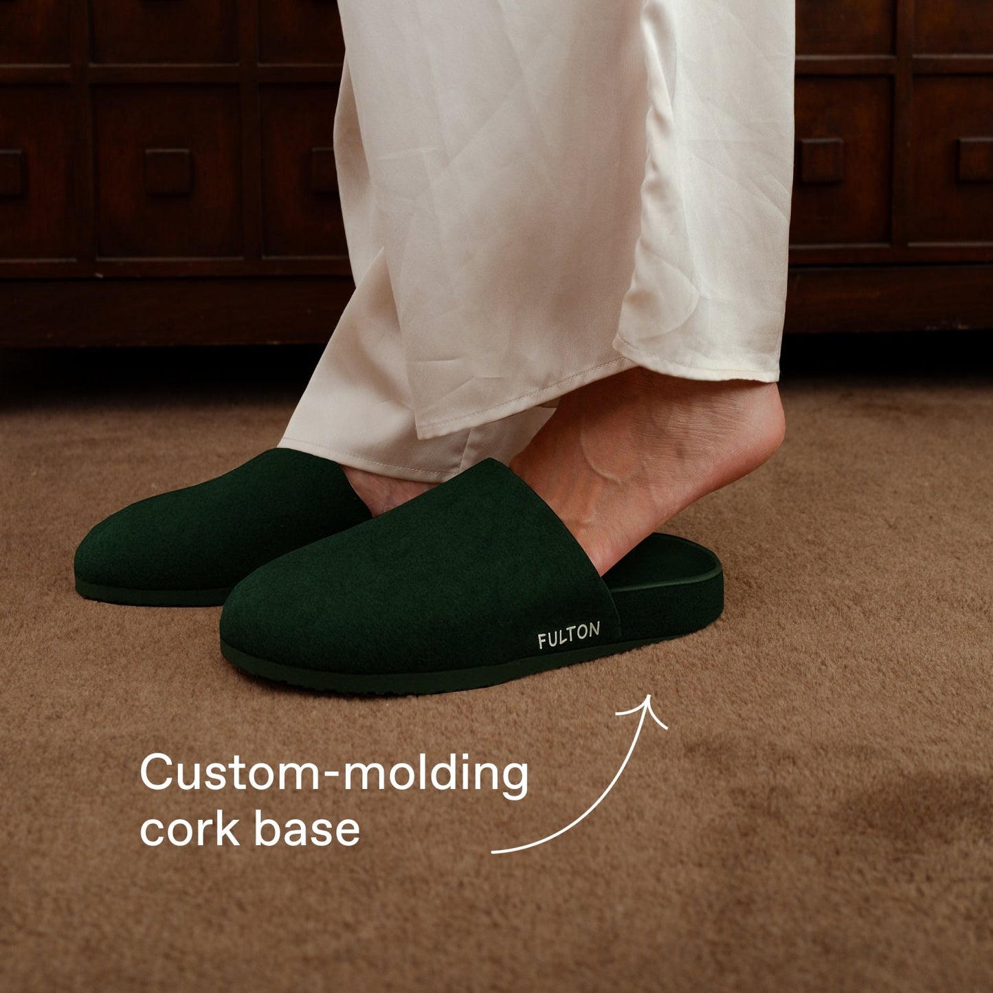 Dark green house slippers worn with white pants and slip-on design