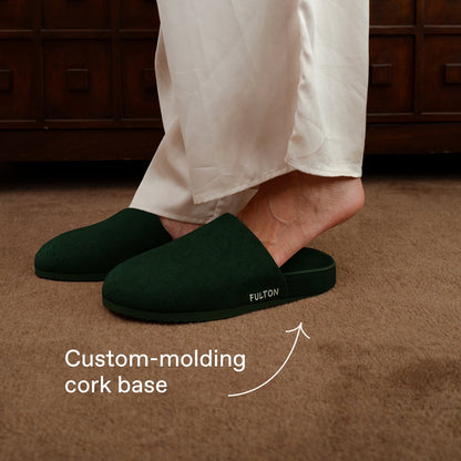 Dark green house slippers worn with white pants and slip-on design