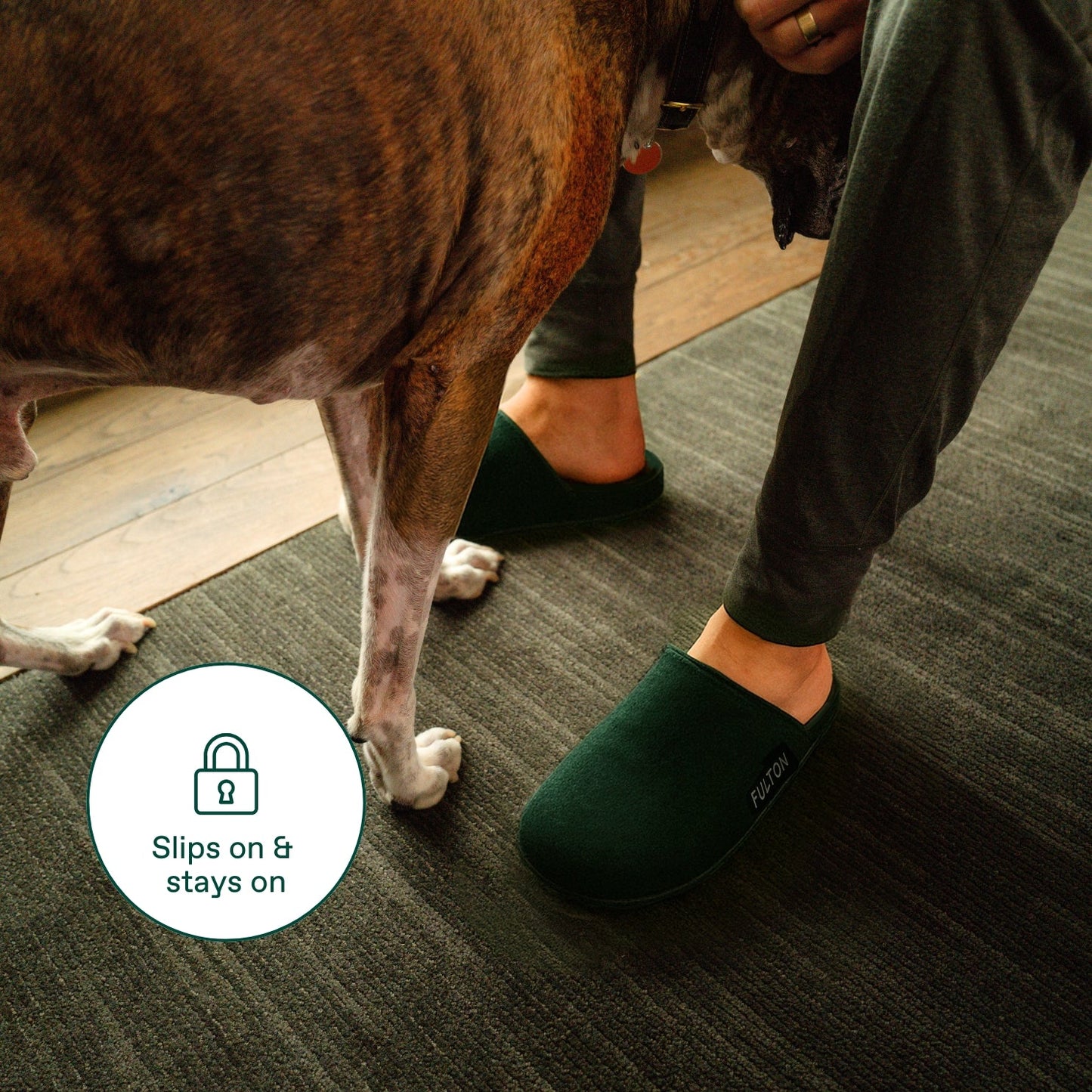 Forest green house slippers on feet with grippy design, open heel and FULTON logo.