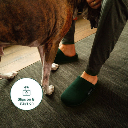 Forest green house slippers on feet with grippy design, open heel and FULTON logo.