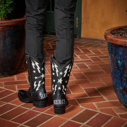 Black cowboy boots with white star-and-lightning patterns and “MERCY” on heel