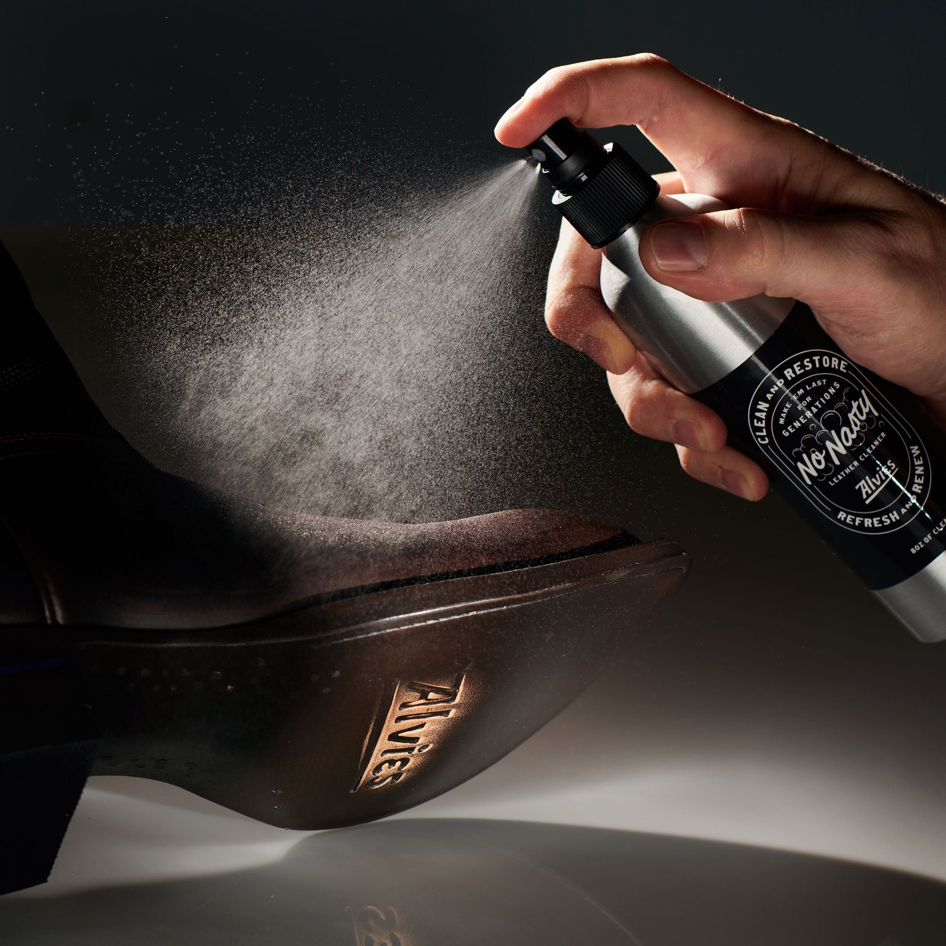 Leather boot cleaner spray misting dark leather boot with hand