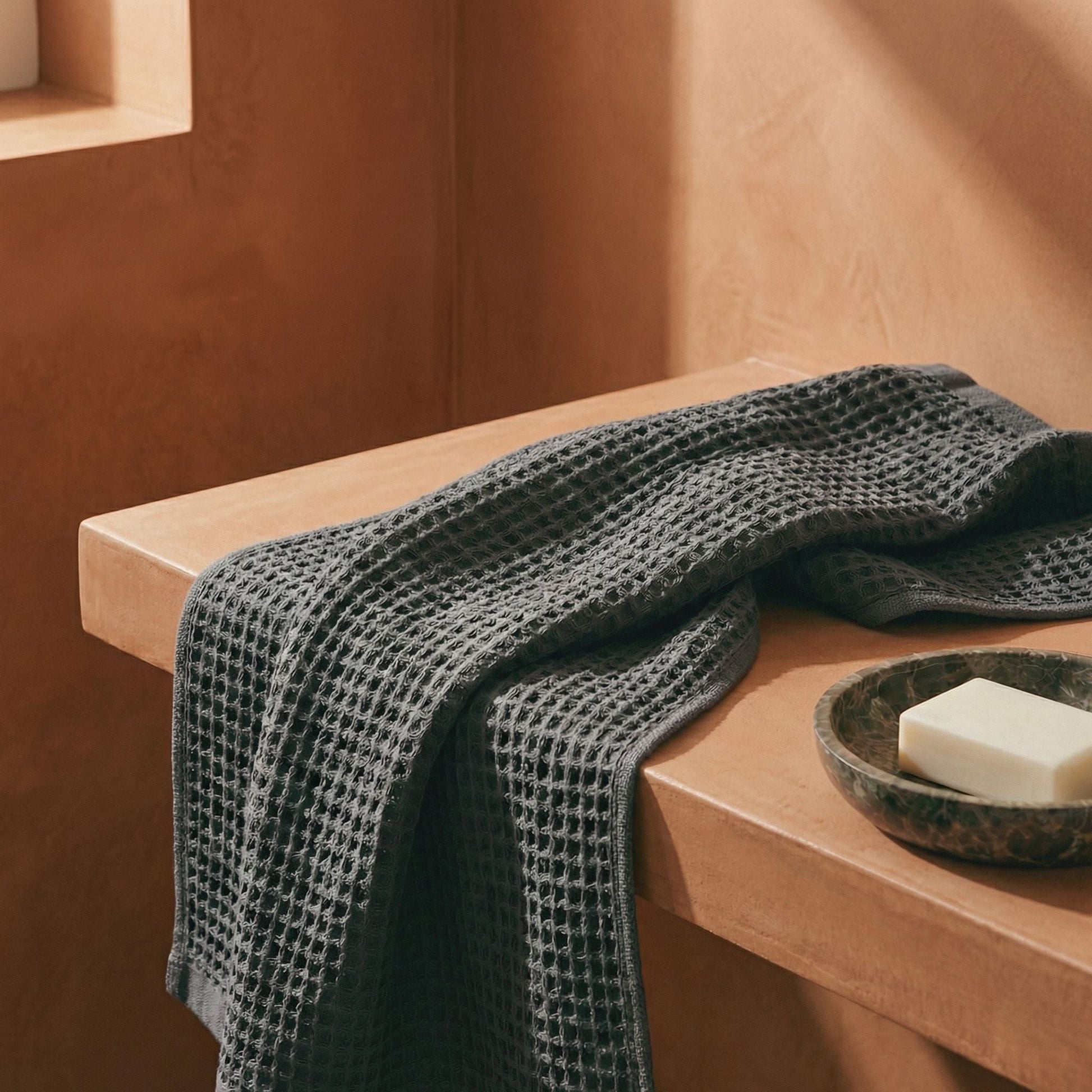 Charcoal waffle cotton towel folded over a ledge, showing textured weave