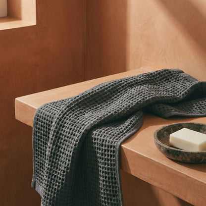 Charcoal waffle cotton towel folded over a ledge, showing textured weave