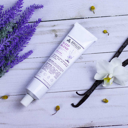 Sleep Blend hand lotion tube lying on flat surface with white cap and vanilla flowers