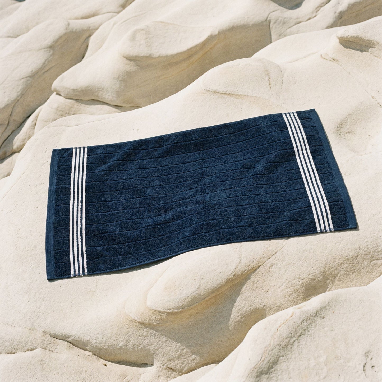 Navy cotton hand towel with white striped bands laid flat on stone