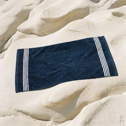 Navy cotton hand towel with white striped bands laid flat on stone