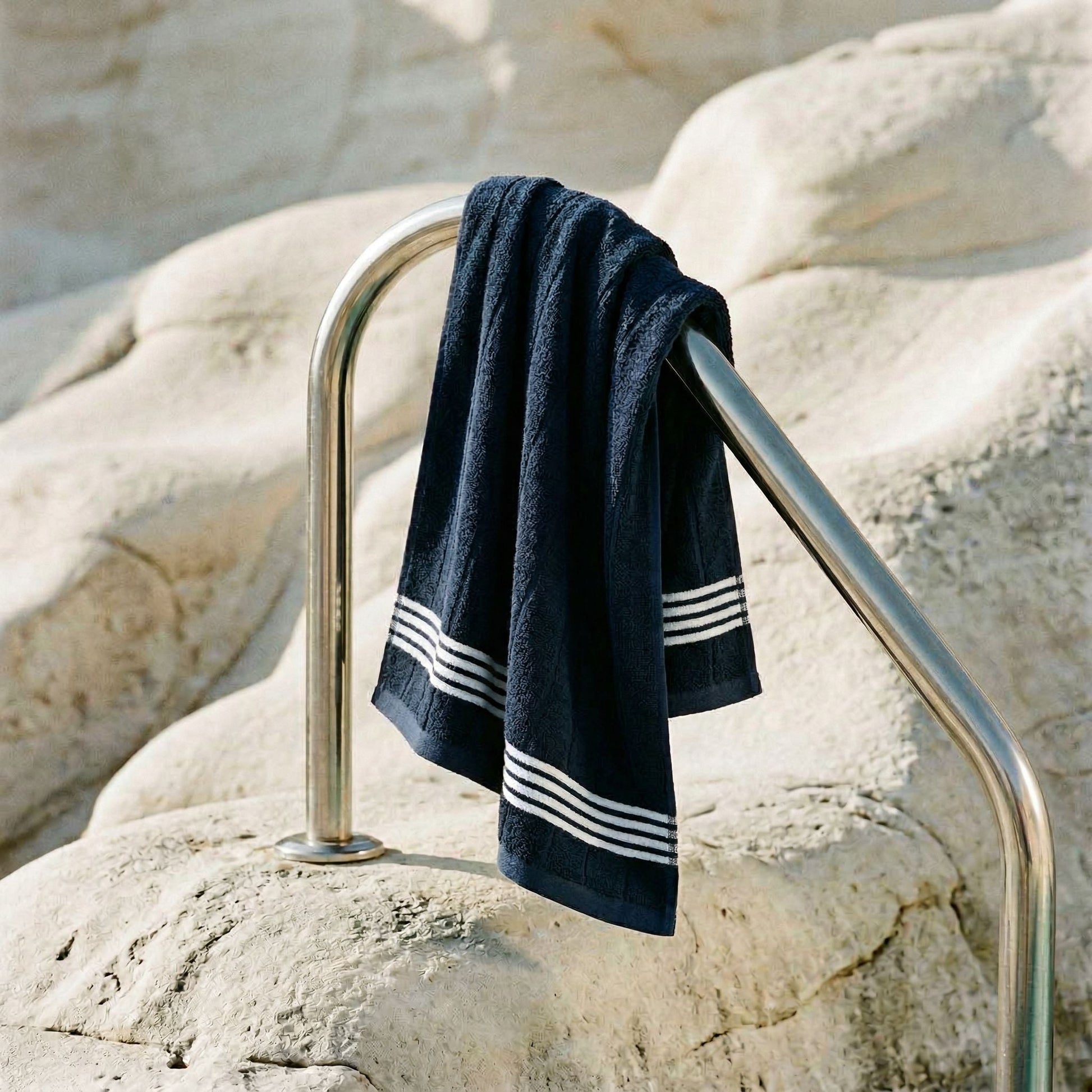 Navy cotton towel with white striped bands draped over a metal rail